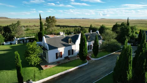 white-cape-cod-style-single-story-family-home-in-valley-of-Karoo-farmlands-in-South-Africa,-aerial