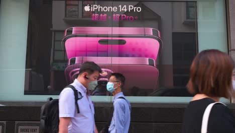 Peatones-Con-Máscaras-Faciales-Pasan-Frente-A-Un-Anuncio-Comercial-De-La-Empresa-Multinacional-Estadounidense-De-Tecnología-Apple-Que-Muestra-El-Teléfono-Inteligente-Iphone-14-Pro-En-Hong-Kong