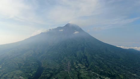 Majestic-volcano-Mount-Merapi-peak-over-serene-Wonolelo-village,-Indonesia,-aerial-view