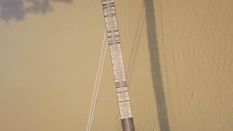 Top-Down-Drone-Shot-from-a-suspension-bridge-over-a-large-river-while-a-motorcyclist-drives-over-it-in-Central-Java-Indonesia