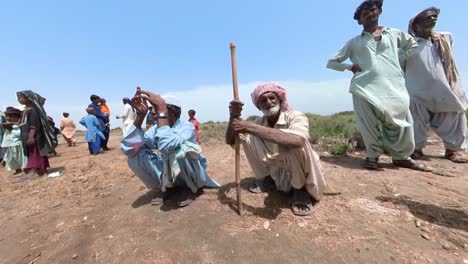 Pair-Of-Elderly-Farmers-Waiting-Sitting-Down-On-Ground-At-Flood-Relief-Camp-In-Sindh,-Pakistan