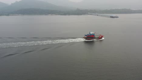 Aerial-drone-following-close-to-a-traditional-fishing-boat-with-foamy-wake,-capturing-hard-working-fisherman-out-on-the-sea-for-a-catch-on-a-foggy-and-misty-morning,-lumut,-manjung,-perak,-malaysia