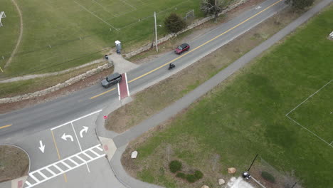 Drone-follow-shot-of-a-motorcycle-leaving-a-parking-lot-and-driving-down-road
