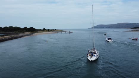 Aerial-view-following-luxury-sailboat-travelling-along-scenic-river-estuary