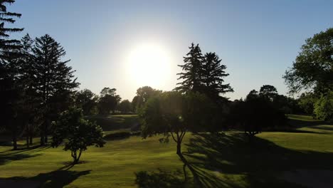 Rising-Shot-of-Golf-Flag-Silhouette-During-Sunset-with-Lens-Flare,-Realtime-Drone-Shot