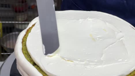 Pastry-chef-using-spatula-to-frost-a-smooth-cake-with-buttercream-meringue-frosting-while-spinning-the-revolving-cake-turntable-stand,-close-up-shot-in-commercial-kitchen-bakery-setting