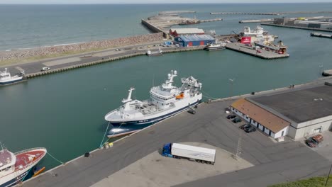 In-this-aerial-view,-the-white-and-blue-colored-fishing-trawler-Linkbank-is-moored-in-the-port-near-the-pier-in-Hanstholm,-Denmark