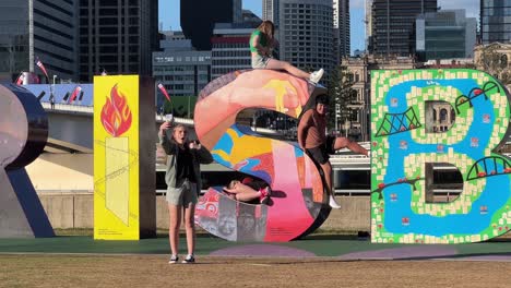 Group-of-teenagers-taking-seflie-with-the-giant-colorful-block-letter-of-Brisbane,-the-iconic-landmark-at-downtown-river-bank-on-a-sunny-day,-Queensland-the-sunshine-state,-Australia,-close-up-shot