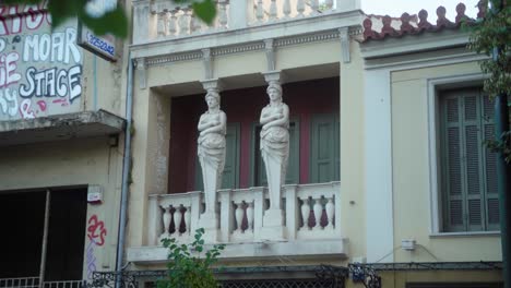 Cerrar-Dos-Estatuas-En-Un-Balcón-Rodeado-De-Graffiti-En-Las-Paredes-En-Atenas,-Grecia