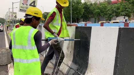 Trabajadores-De-La-Construcción-Perforando-Agujeros-En-Un-Divisor-De-Carreteras-En-Una-Carretera-Muy-Transitada