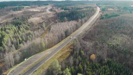 Aerial,-tilt-down,-drone-shot,-flying-towards-cars-on-a-road-and-leafless-autumn-forest,-on-a-sunny-fall-day,-in-Juuka,-Pohjois-Karjala,-Finland