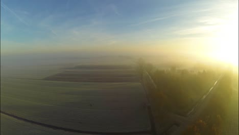 Aerial-of-sunrise-through-fog-above-a-frozen-landscape