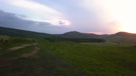 Aerial-view-of-a-wide-valley-while-the-sun-is-setting-behind-the-mountains-in-the-background,-Transylvania,-Romania---Pan