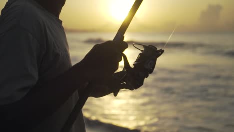 Cerrar-La-Caña-De-Pescar-Sostenida-Por-Un-Pescador-Indonesio-Pescando-En-La-Costa-De-Un-Océano-O-Un-Mar-Al-Atardecer-O-Al-Amanecer