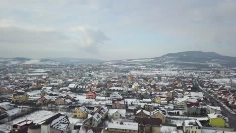 Drone-flying-over-suburbs-of-city-with-colorful-houses-and-snow-covered-roofs,-Bistrita,-Romania,-forward-dolly-move