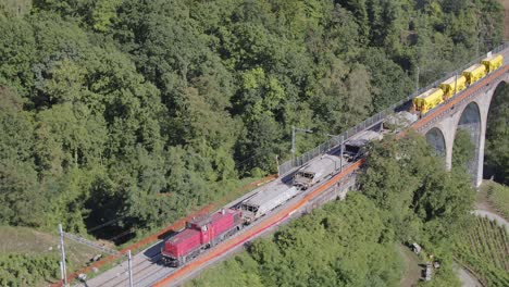Aerial-view-of-freight-train-laying-ballast-passing-slowly-over-viaduct-Pont-de-Bory,-Lavaux---Switzerland