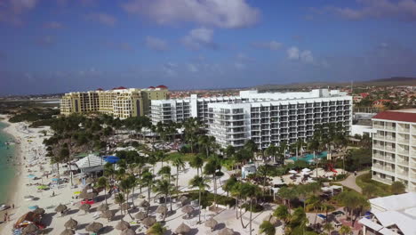 Hoteles-De-Gran-Altura-Con-Palmeras-Que-Soplan-En-El-Viento-A-Lo-Largo-De-La-Playa-En-Aruba