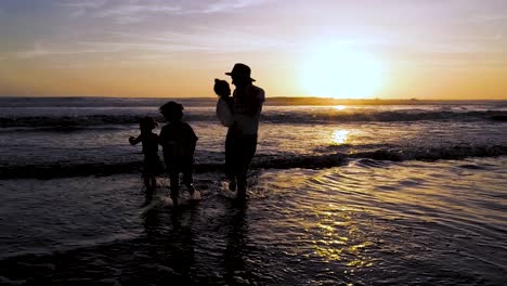 Eine-Mutter-Rennt-Mit-Ihren-Drei-Kindern-Bei-Sonnenuntergang-Am-Strand-In-Zeitlupe