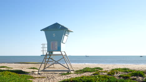 A-lifeguard-tower-on-the-sandy-beach-with-ocean-waves-crashing-on-the-shore-in-slow-motion-in-Santa-Barbara,-California