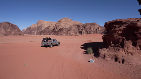 Ein-Auto-Mit-Touristen-Im-Kofferraum-Fährt-über-Sand-In-Die-Dünen-Der-Wüste-Wadi-Rum
