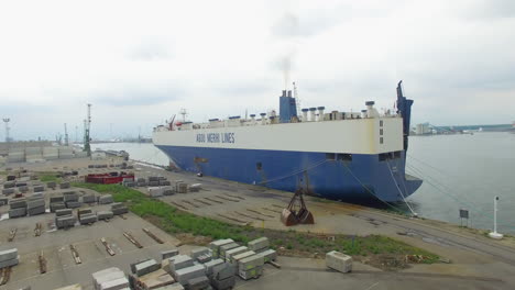 Flying-towards-a-big-cargo-ship,-surrounded-by-machinery,-granite-blocks-and-windmills