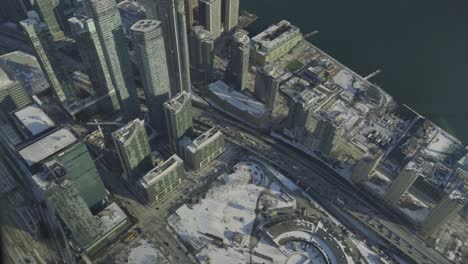 Aerial-view-of-downtown-Toronto-with-large-skyscrapers,-snow-covered-ground-and-a-half-frozen-Lake-Ontario-on-a-cold-winters-day
