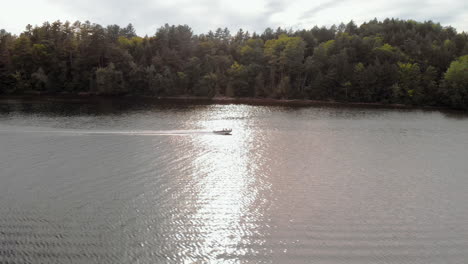 Pan-right-tracking-speedboat-moving-across-blue-lake-with-forest-of-trees