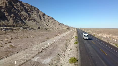 Aerial,-reverse,-drone-shot,-of-a-camper-rv,-truck,-driving-on-a-desert-road,-on-a-sunny-day,-on-San-Felipe-highway,-in-Baja,-California,-Mexico