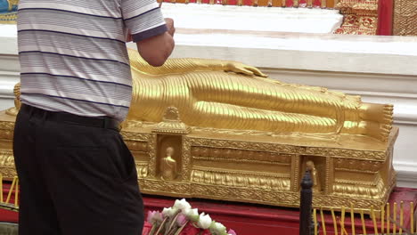 Un-Hombre-Haciendo-Una-Oferta-A-Una-Estatua-De-Buda-Mentirosa,-Tailandia