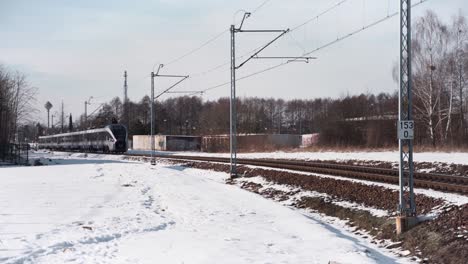 Medium-wide-shot-of-an-electric-passenger-train-leaving-a-town-covered-with-snow-during-winter-in-daytime