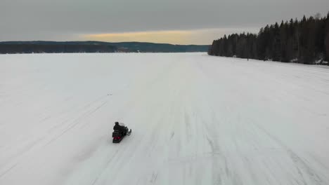 Tracking-aerial-shot-of-a-man-driving-his-snowmobile-on-Indalsalven-in-Timra,-Sundsvall,-Sweden