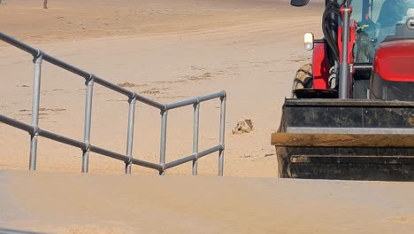 Mann-Fährt-Mit-Rotem-Traktor-Am-Sandstrand-Die-Betonrampe-Hinauf,-Nahaufnahme-Der-Vorbeifahrenden-Reifen