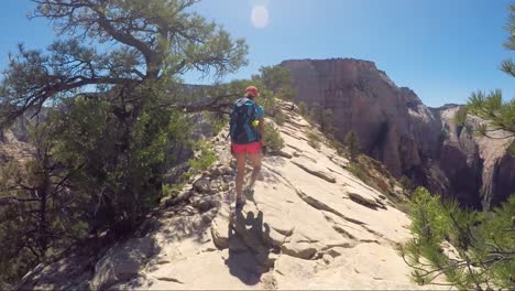 Young-woman-wearing-backpack-is-walking-on-the-ridge-to-Angel's-Landing-in-Zion-National-park-in-Utah,-USA