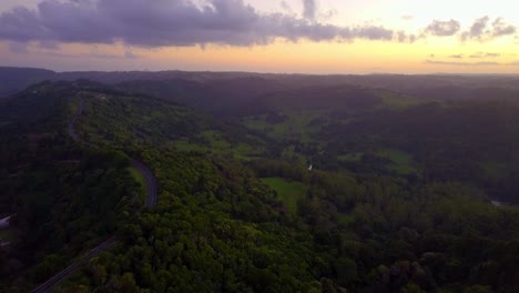 Aerial-view-of-hills-and-road-in-a-tropical-forest-valley-at-sunset