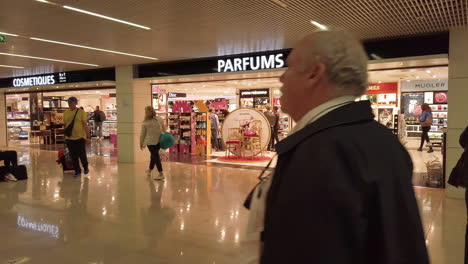 Pasajeros-En-El-Interior-Del-Aeropuerto-De-Orly-Camino-Al-Embarque-Y-Al-Paso-Frente-A-Las-Tiendas-Libres-De-Impuestos