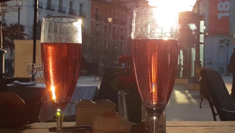 Sonnenstrahlen-Treffen-Auf-Prickelnden-Roséwein-Im-Außenterrassenrestaurant-In-Madrid,-Festliche-Seifenblasen-Steigen-Auf