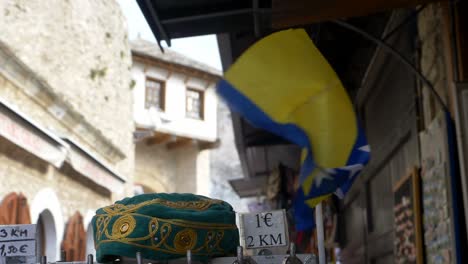 Kleine-Flagge-Von-Bosnien-Und-Herzegowina,-Die-Im-Wind-Neben-Einer-Traditionellen-Schädeldecke-Oder-Taqiyah-Flattert