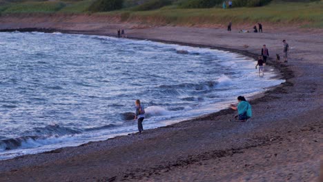 Glückliche-Mutter-Und-Tochter-Genießen-Und-Fotografieren-Den-Romantischen-Sonnenuntergang-Am-Meer,-Weitwinkelaufnahme-Aus-Der-Ferne