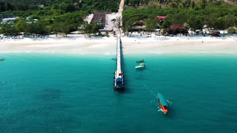 Aerial-shot-of-long-tail-boat-leaving-wooden-pier-from-4k-Beach,-Kong-Rong,-Cambodia