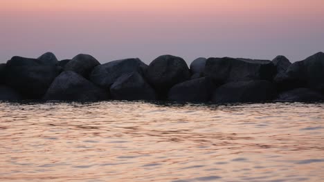 Sunset-over-water-sea,-line-of-rocks-in-water,-dusk-light