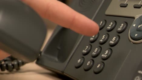 A-close-up-of-a-desk-office-phone-while-a-hand-pushes-buttons,-removes-the-receiver-and-places-it-back-on-the-base-in-slow-motion