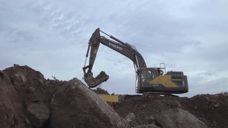 Volvo-excavator-loading-a-tipper-dumper-with-stone-and-gravel-in-muddy-environment,-Long-shot