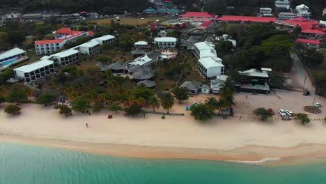 Aerial-shot-of-a-resort-along-Grand-Anse-Beach-with-a-small-strip-mall-in-the-background