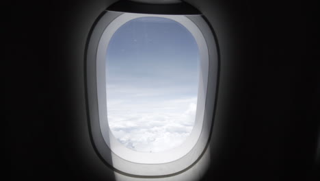 Slow-motion-dolly-out-or-pullout-of-a-plane-window-in-the-cabin-with-amazing-blue-sky-and-white-clouds