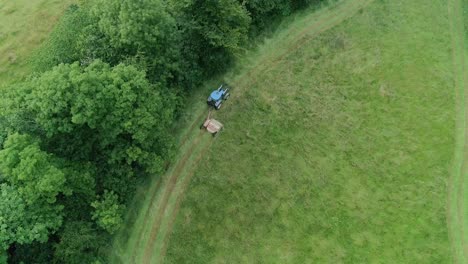 Top-down-aerial-rising-to-reveal-a-tractor-cutting-the-grass-around-the-edge-of-an-unusually-shaped-field