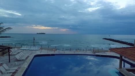 Vista-Aérea-Con-Drones-Volando-Sobre-Una-Piscina-Y-El-Mar,-Desde-Un-Hotel-De-Playa