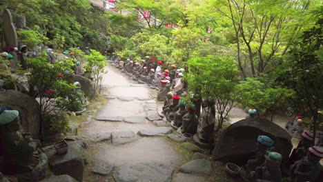 Small-Buddha-statues-with-woolly-hat-on-a-path-of-the-Daisho-in-Buddhist-temple-site-on-the-on-Miyajima-Island,-prefecture-of-Hiroshima