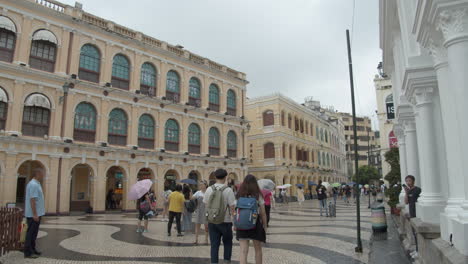 Senado-Square-with-colorfully-painted-buildings-and-tourists-passing-by-on-a-gray-cloudy-overcast-day-in-Macau,-Macau-SAR,-China