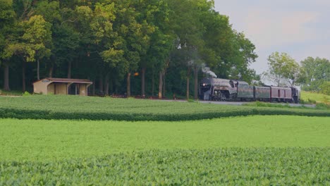 Una-Vista-Aérea-De-Un-Tren-De-Vapor-No-611-Que-Sopla-Humo-A-Través-Del-Campo-Agrícola-En-Un-Día-Soleado-De-Verano-Con-Campos-Verdes