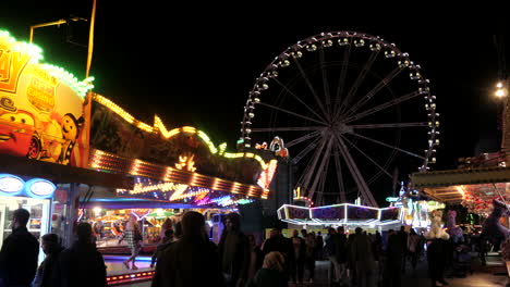 Happy-peoples-strolling-over-fun-fair-event-at-night,-wide-pan-right-shot